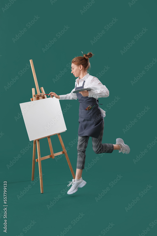 Young female artist with tools jumping on green background