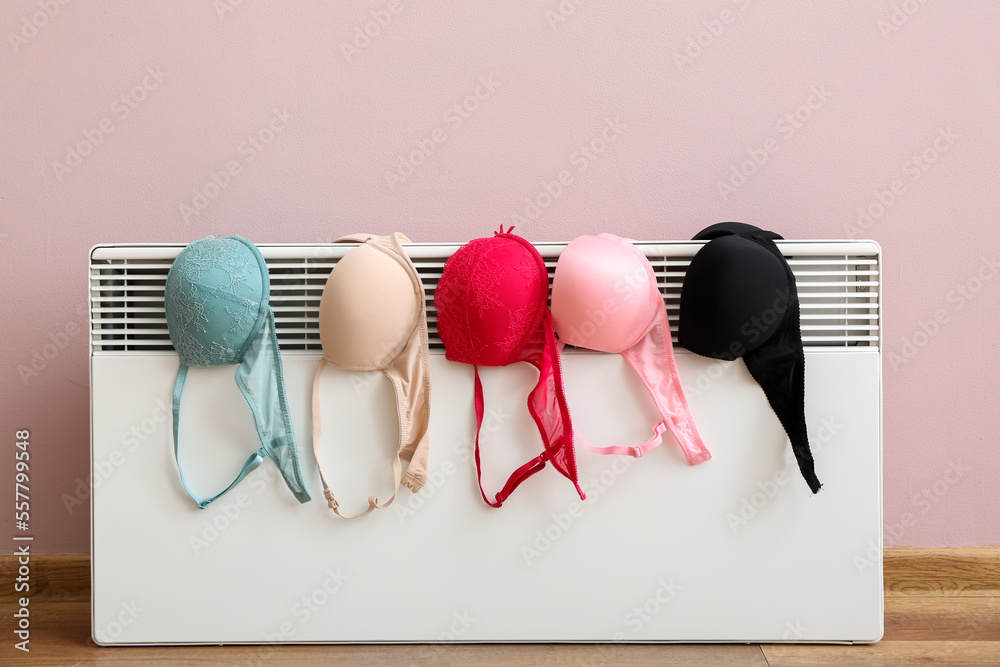 Female bras drying on electric radiator near pink wall