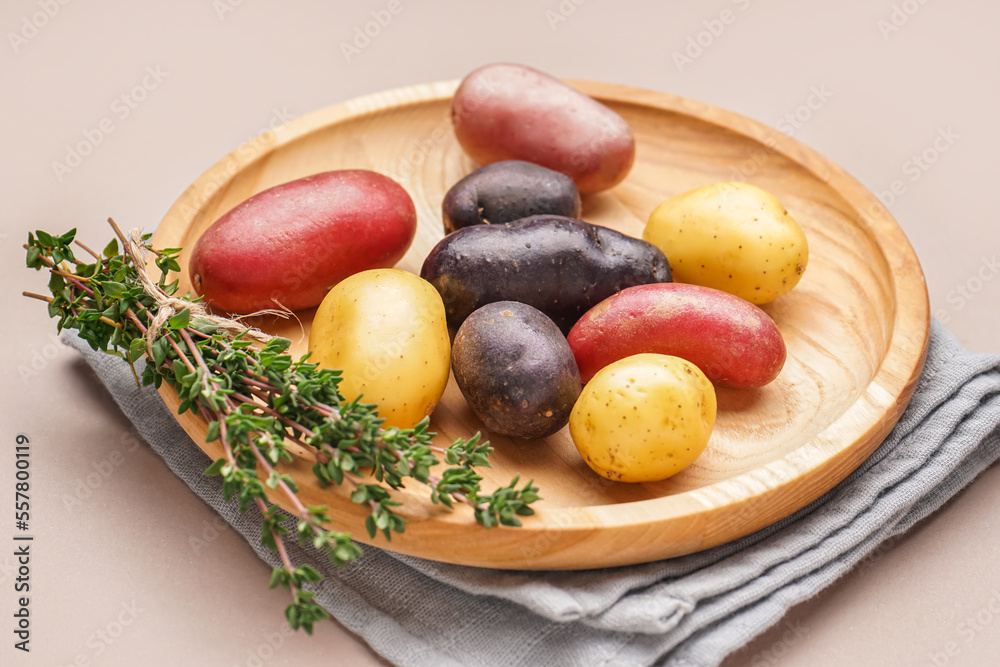 Wooden plate with different raw potatoes and thyme on color background