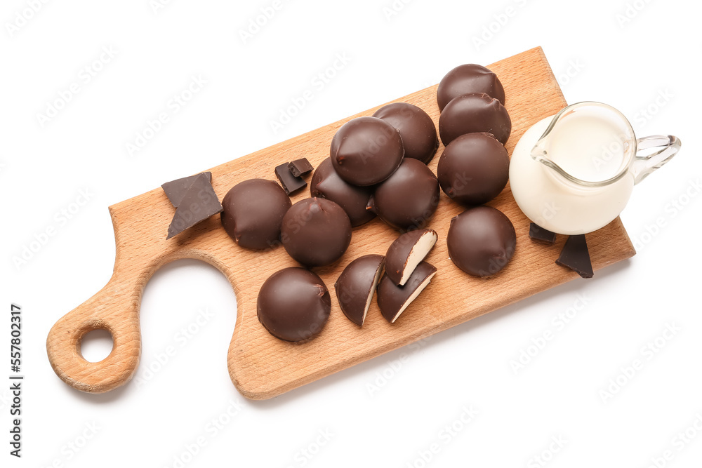 Cutting board with sweet chocolate birds milk candies and pitcher of milk on white background