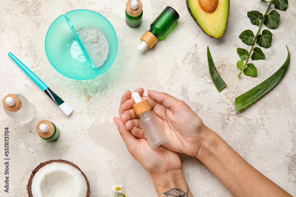 Female hands with bottle of essential oil and different natural ingredients on light background