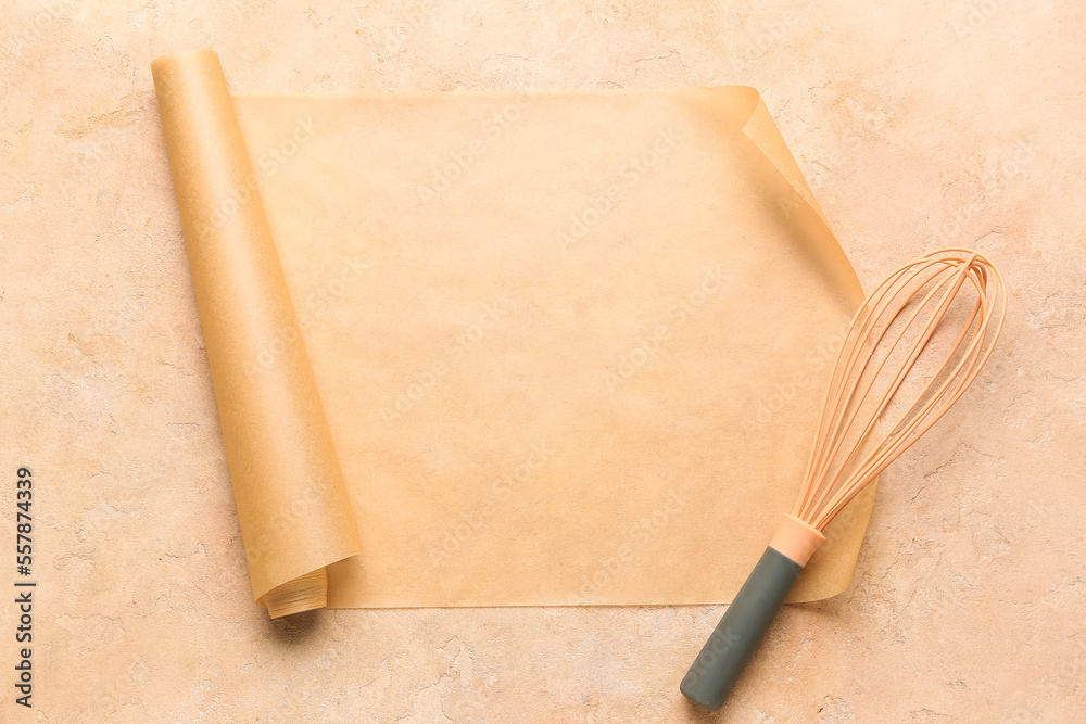 Roll of baking paper and whisk on beige background