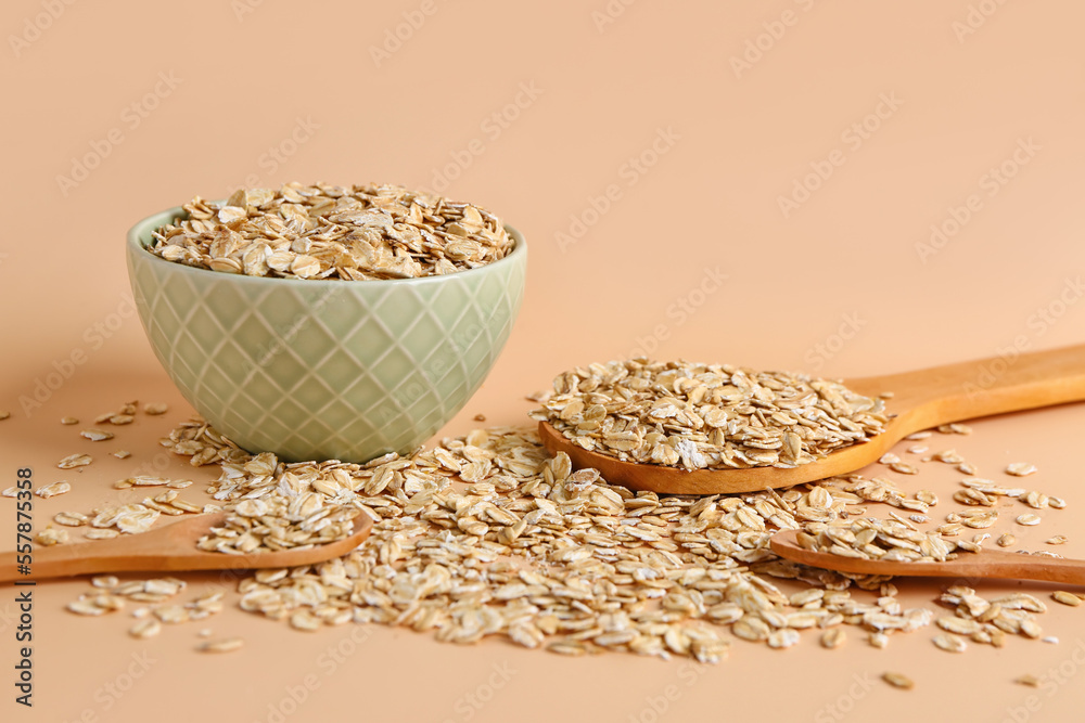 Bowl and spoons of raw oatmeal on color background