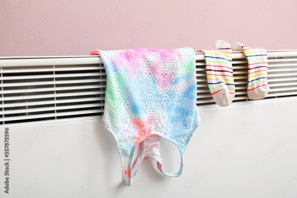 Warm socks and top drying on electric radiator near pink wall, closeup