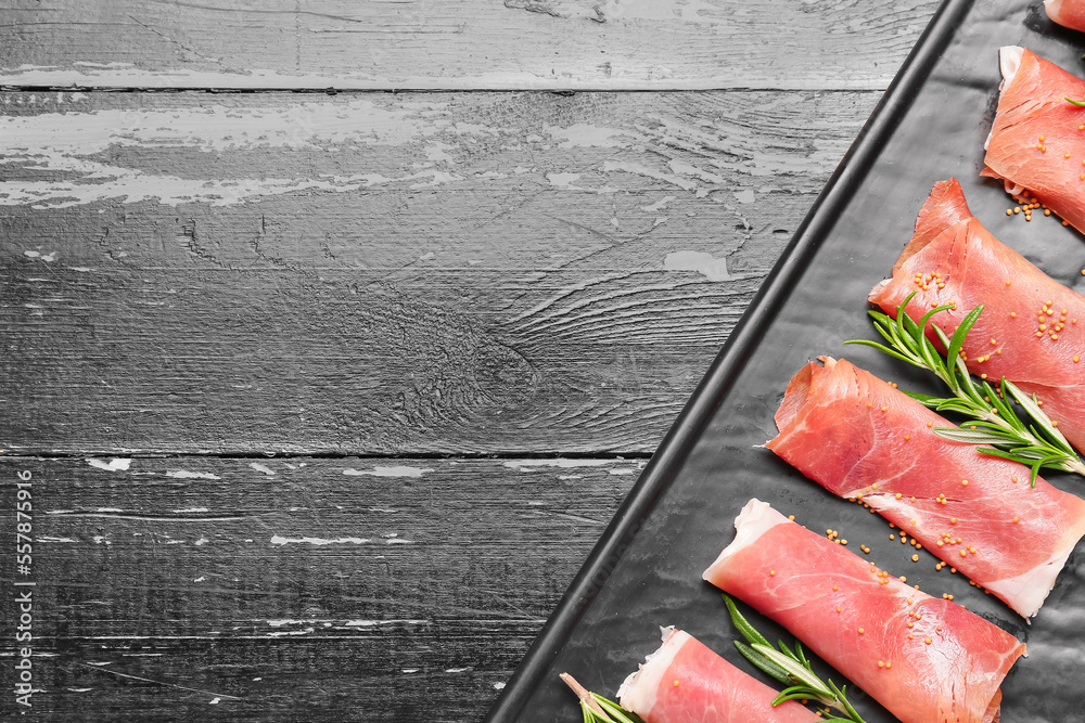 Plate with slices of tasty ham and rosemary on dark wooden background