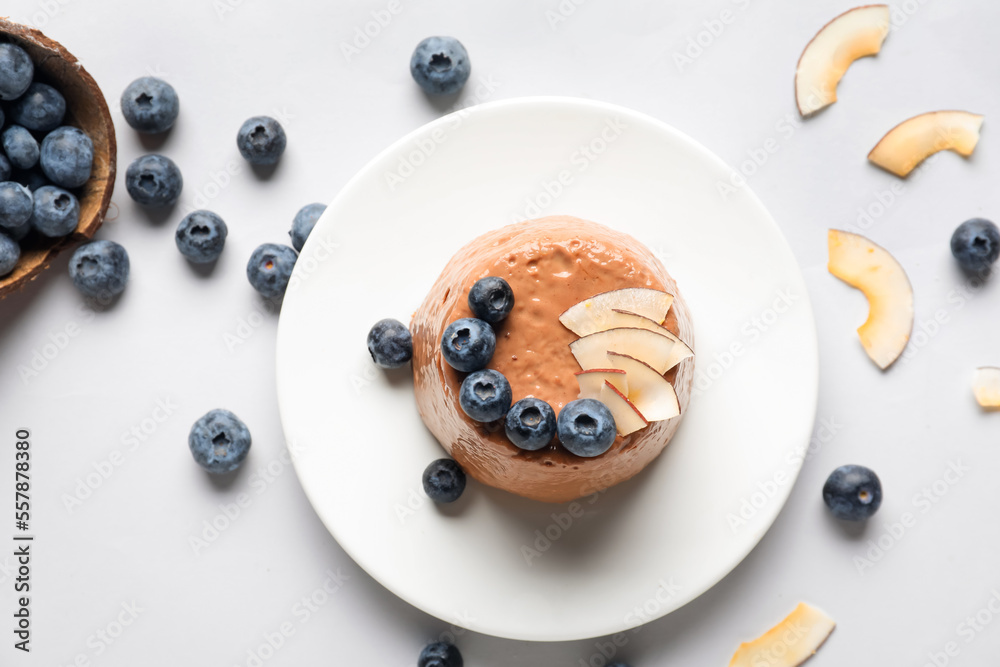 Plate with delicious chocolate pudding, coconut slices and blueberry on white background