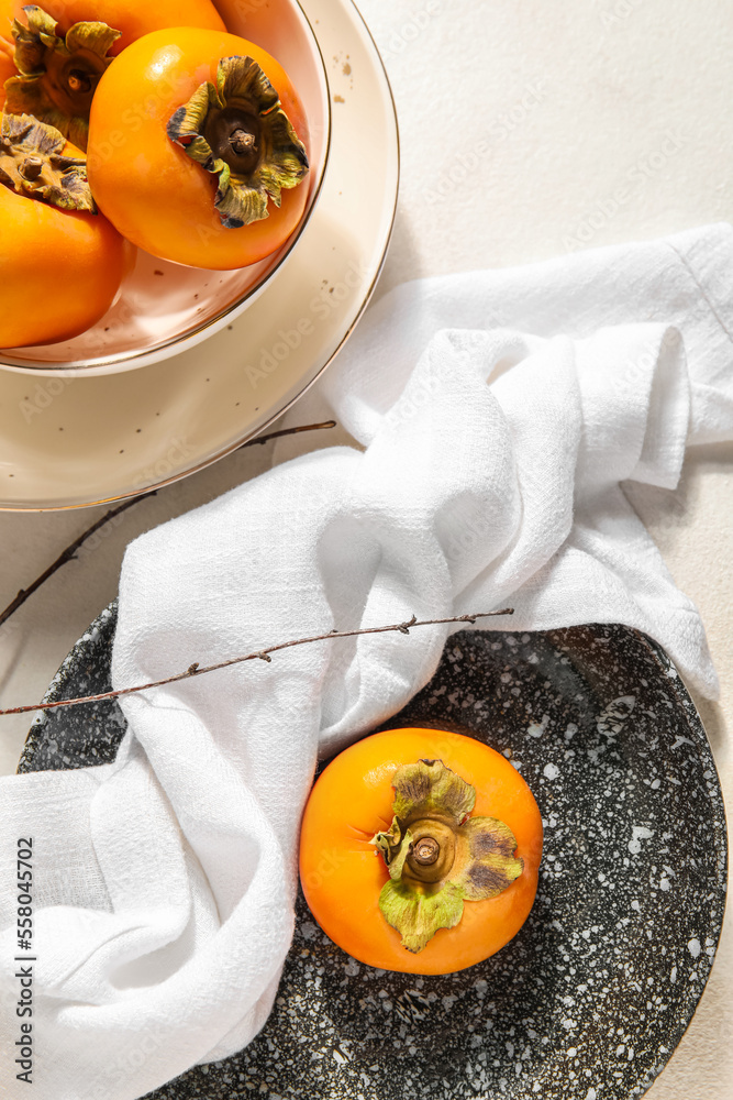 Plates with ripe persimmons on light background, closeup