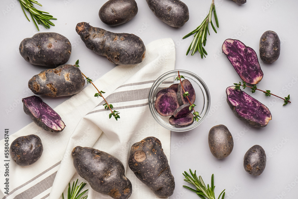 Composition with cut and whole purple potatoes and herbs on white background