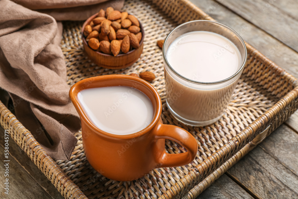 Tray with jug, glass of healthy almond milk and nuts on wooden table, closeup