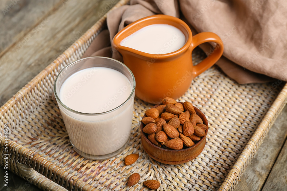 Tray with jug, glass of healthy almond milk and nuts on wooden table, closeup