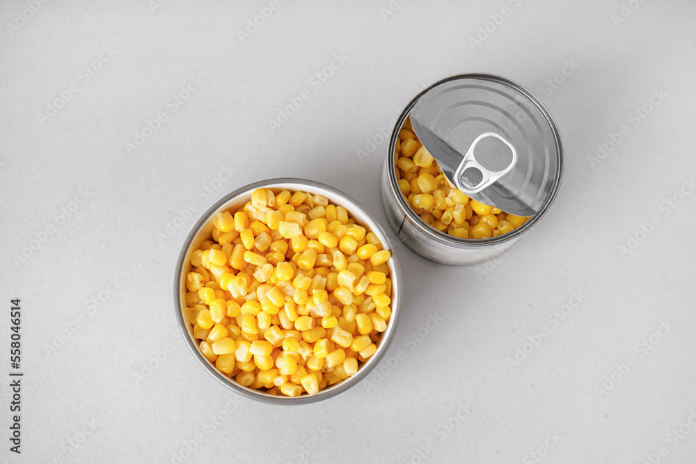 Bowl and tin can with canned corn on grey background