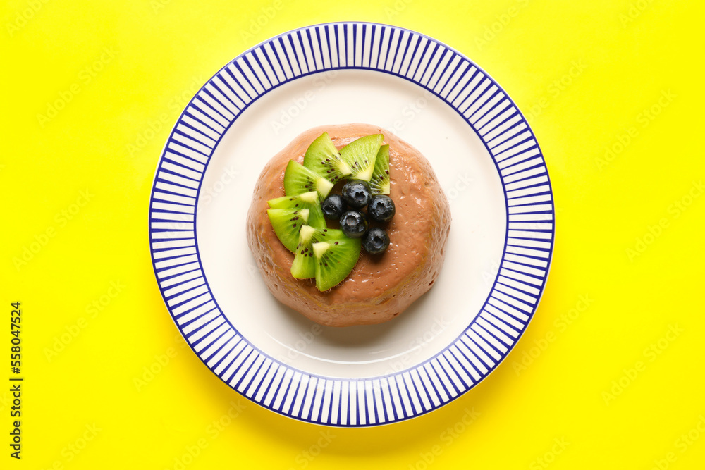 Plate with delicious chocolate pudding, kiwi slices and blueberry on yellow background