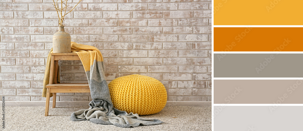 Knitted pouf, stepladder with vase and plaid near light brick wall in room. Different color patterns