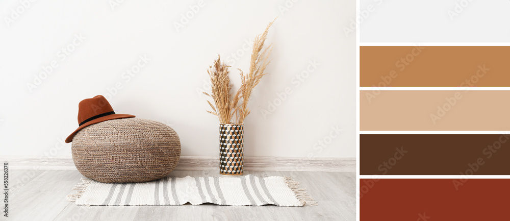 Stylish pouf with hat, vase with floral decor and rug near white wall in room. Different color patte