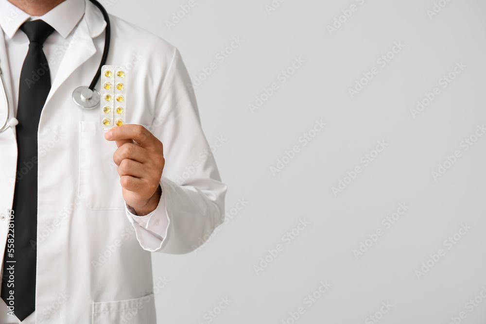 Male doctor with vitamins on light background