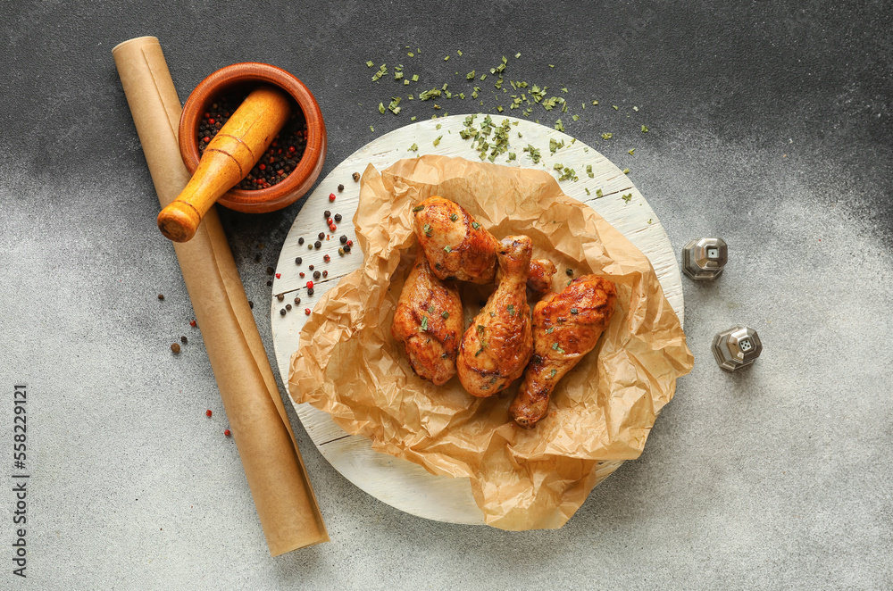 Wooden board with tasty baked chicken legs, spices and roll of baking paper on black and white backg