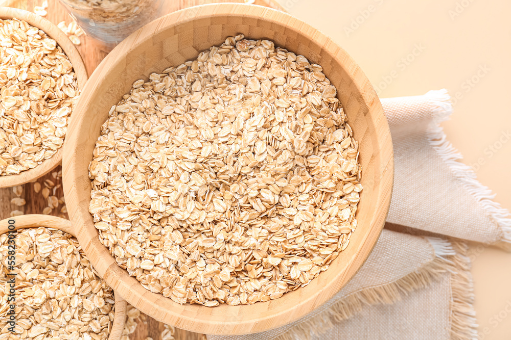 Wooden bowls of raw oatmeal on color background, closeup