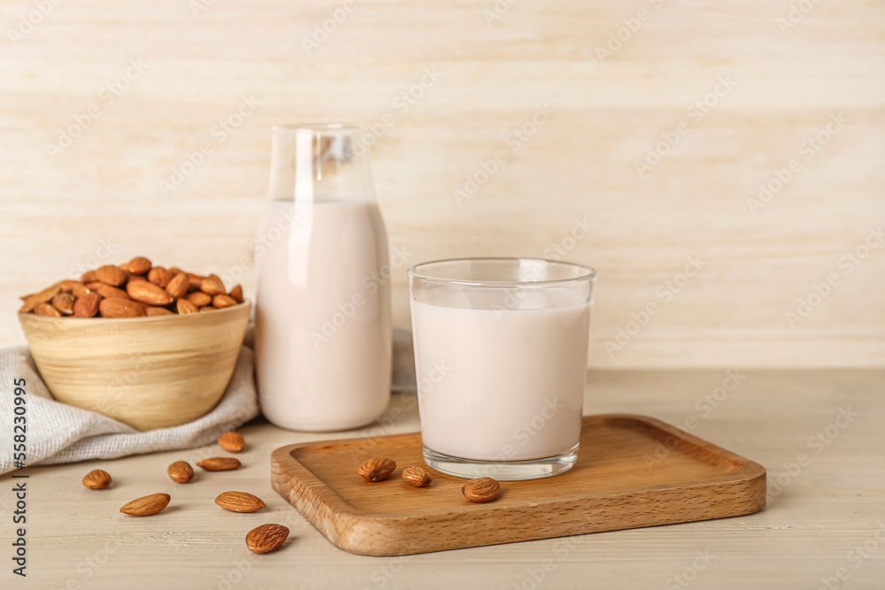 Board with glass of healthy almond milk and nuts on wooden background