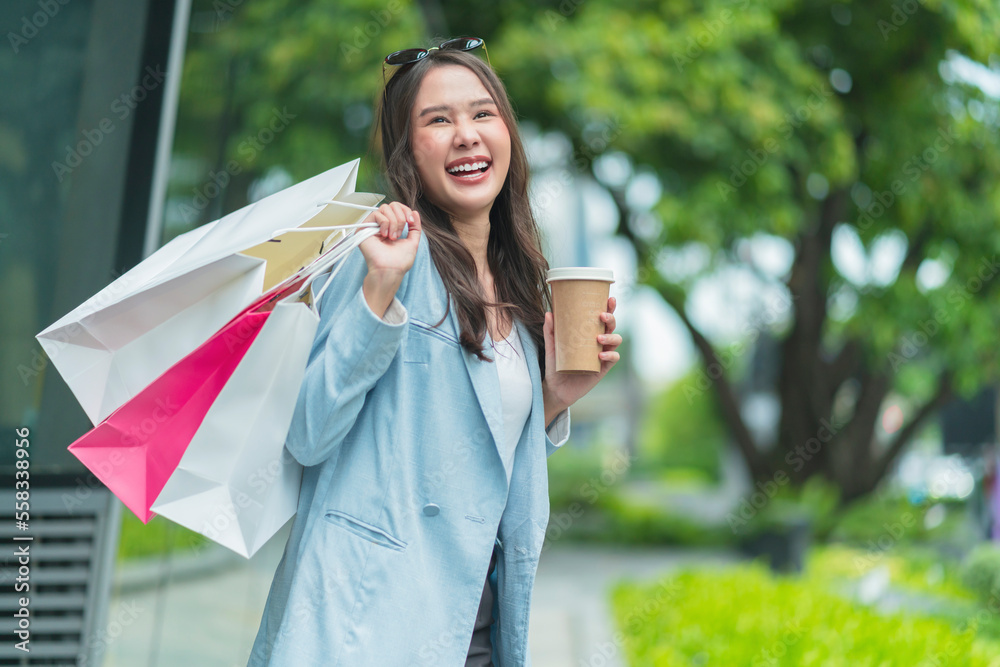 Stylish shopaholic asian teen woman in trendy trench business casual sunglasses in city with shoppin