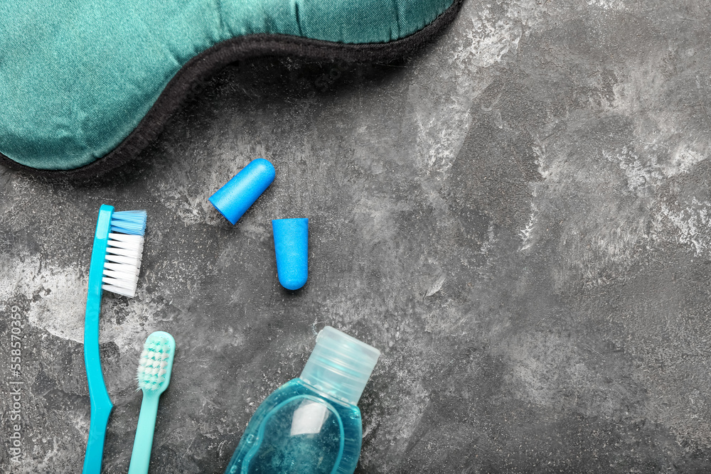 Earplugs, toothbrushes, sleeping mask and bottle of cosmetic product on dark background