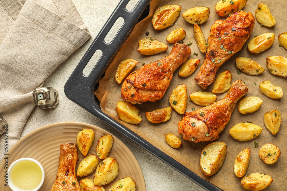 Baking sheet with tasty baked potato and chicken legs on table, closeup