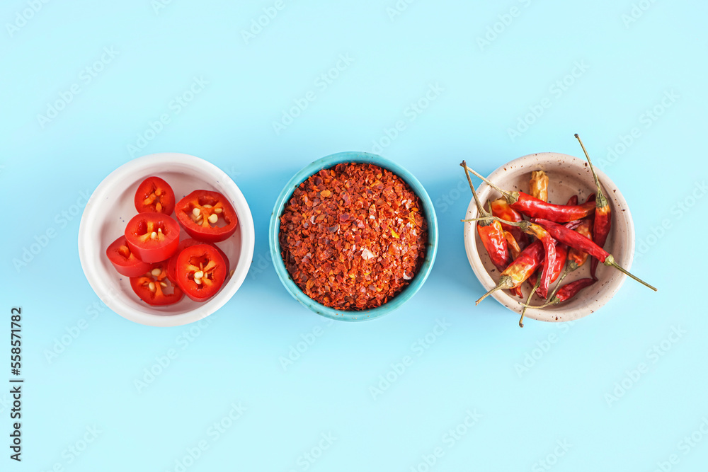 Bowls with chipotle chili flakes, fresh and dried jalapeno peppers on color background