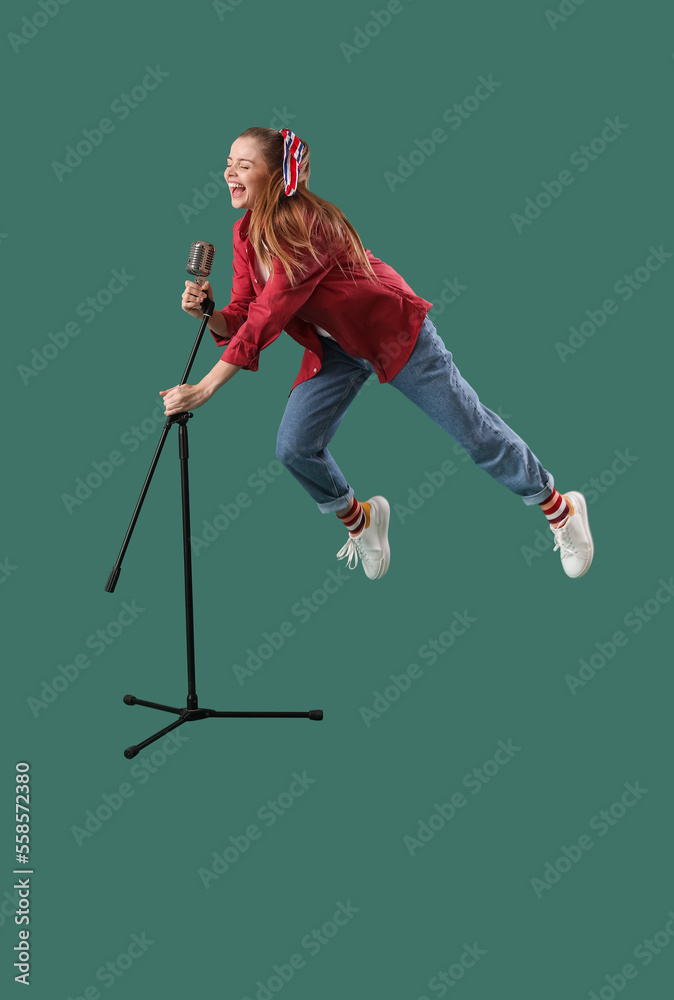 Young female singer with microphone jumping on green background