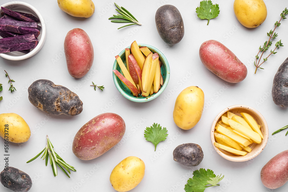 Composition with different types of raw potatoes and herbs on light background