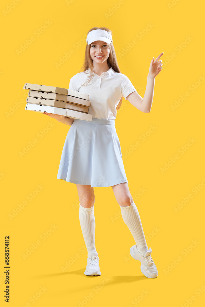 Young woman with boxes of tasty pizza pointing at something on yellow background