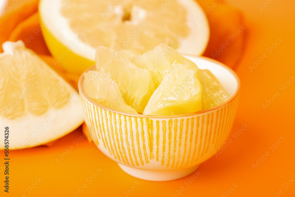 Bowl with slices and halves of pomelo fruit on orange background, closeup