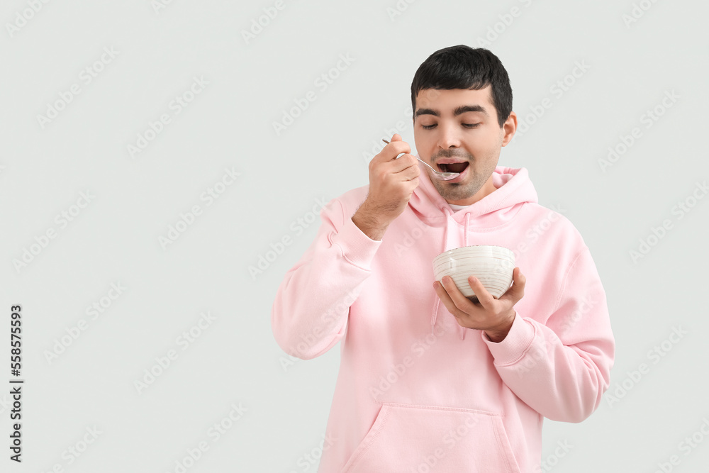 Young man with silver spoon and bowl on grey background