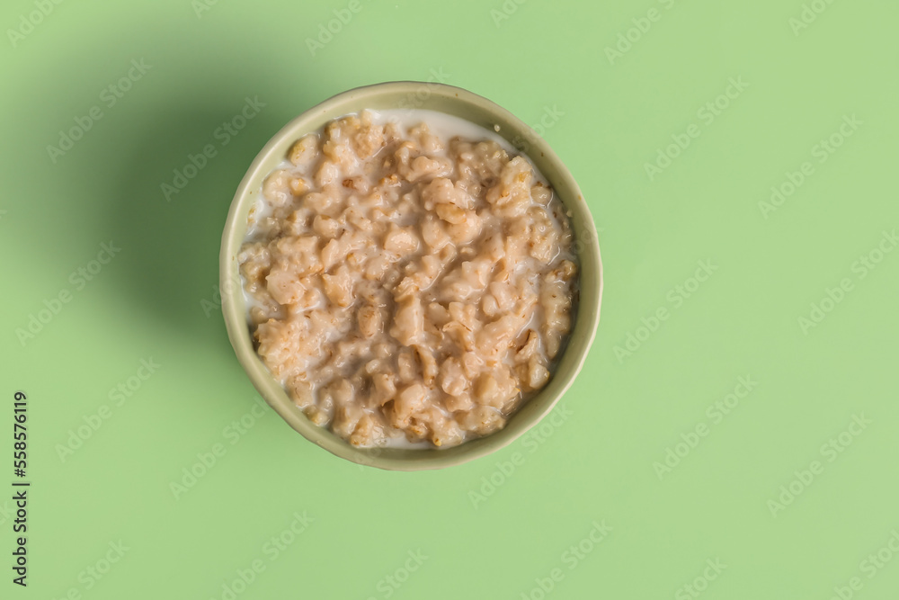 Bowl with tasty oatmeal on green background