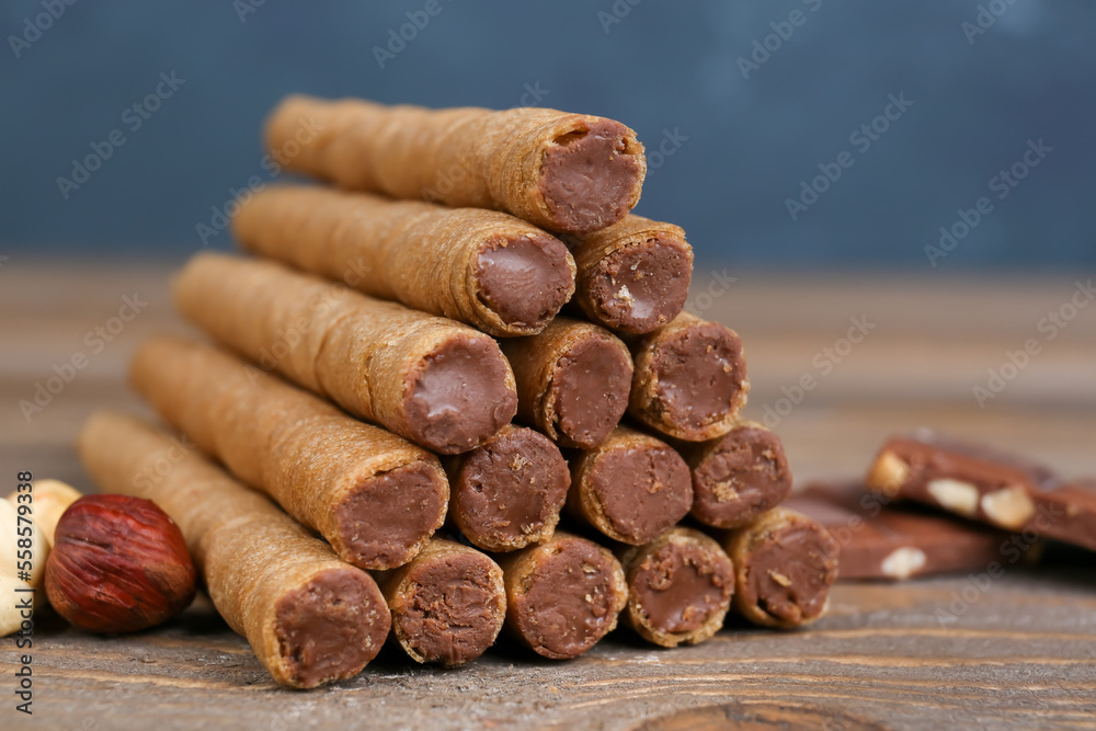 Tasty wafer rolls with boiled condensed milk, chocolate and nuts on wooden background, closeup