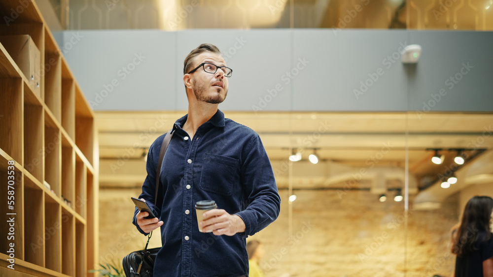 Portrait of a Caucasian Man Walking in Corporate Office with Smartphone and Coffee in His Hands. A B