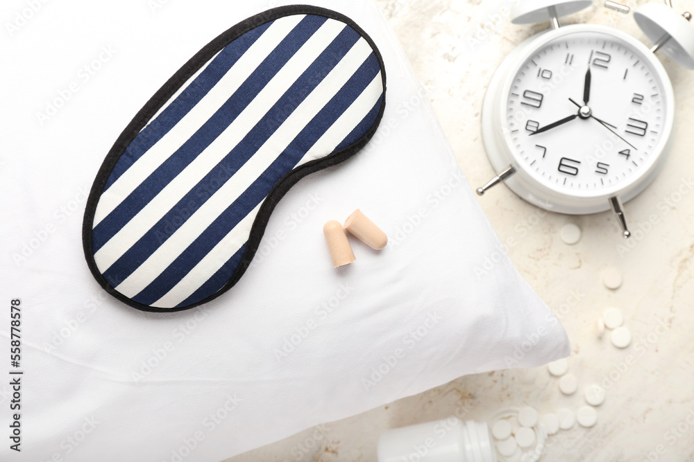 Foam earplugs, sleeping mask, pillow, alarm clock and pills on light background