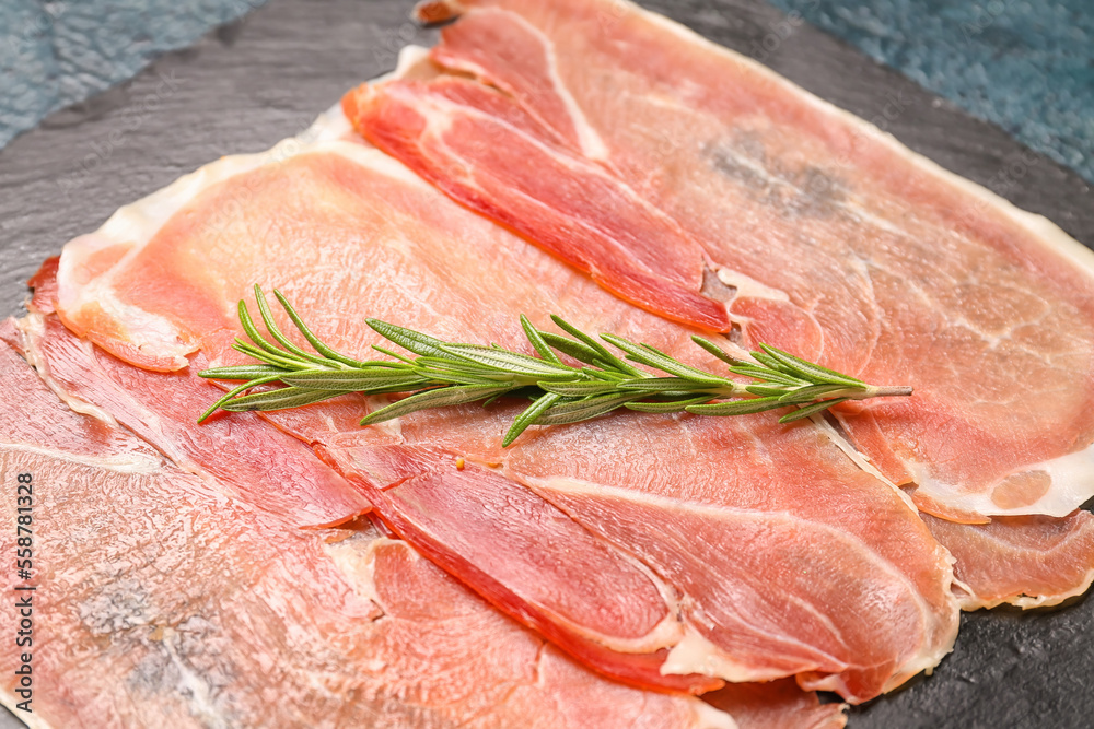 Slate board with slices of tasty ham and rosemary, closeup