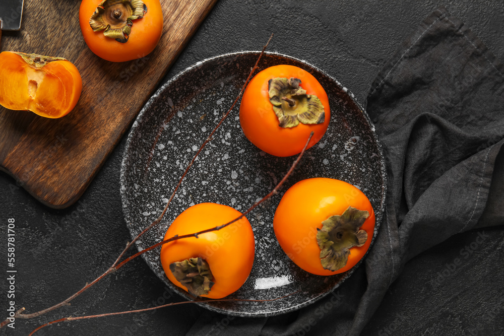 Plate with fresh ripe persimmons on dark background