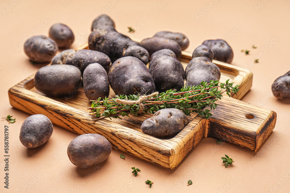 Wooden board with raw purple potatoes and thyme on color background, closeup