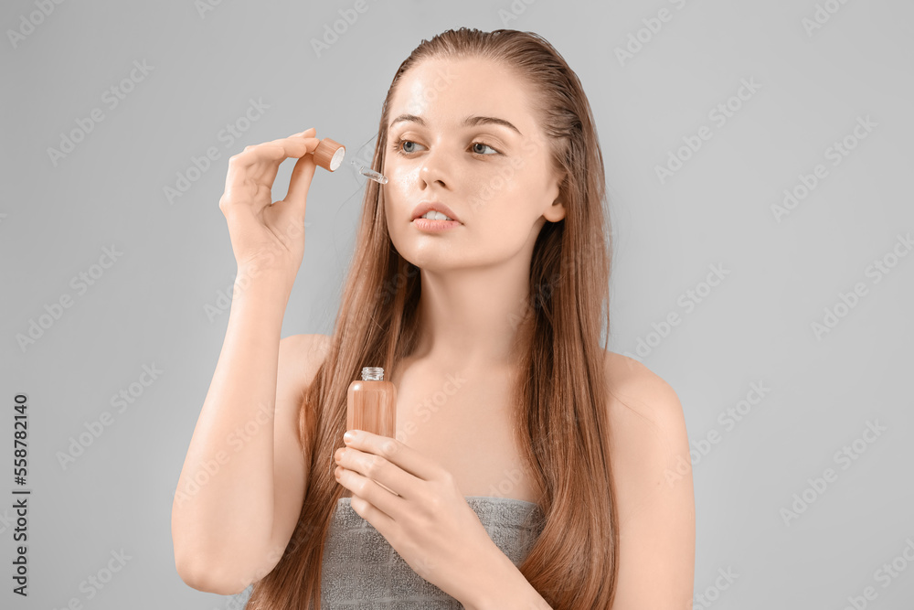 Pretty young woman with cosmetic serum on grey background