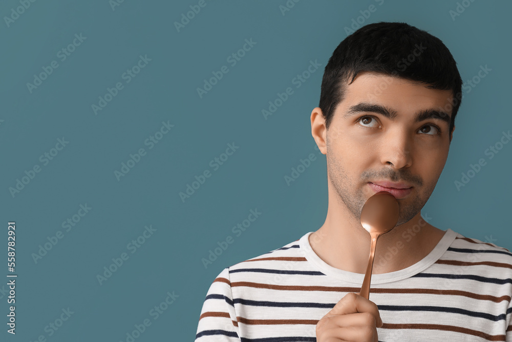 Thoughtful young man with golden spoon on color background, closeup