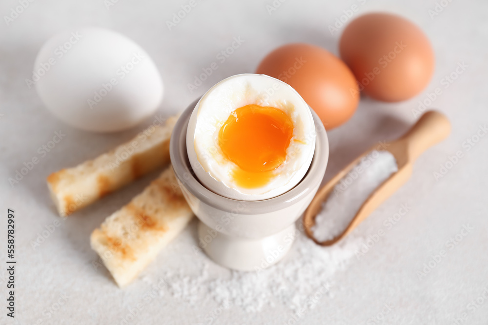 Holder with soft boiled egg, toasted bread and scoop on white table