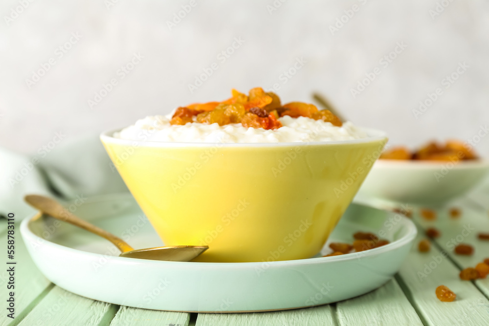 Bowl with delicious rice pudding, raisins, dried apricot and spoon on green wooden table