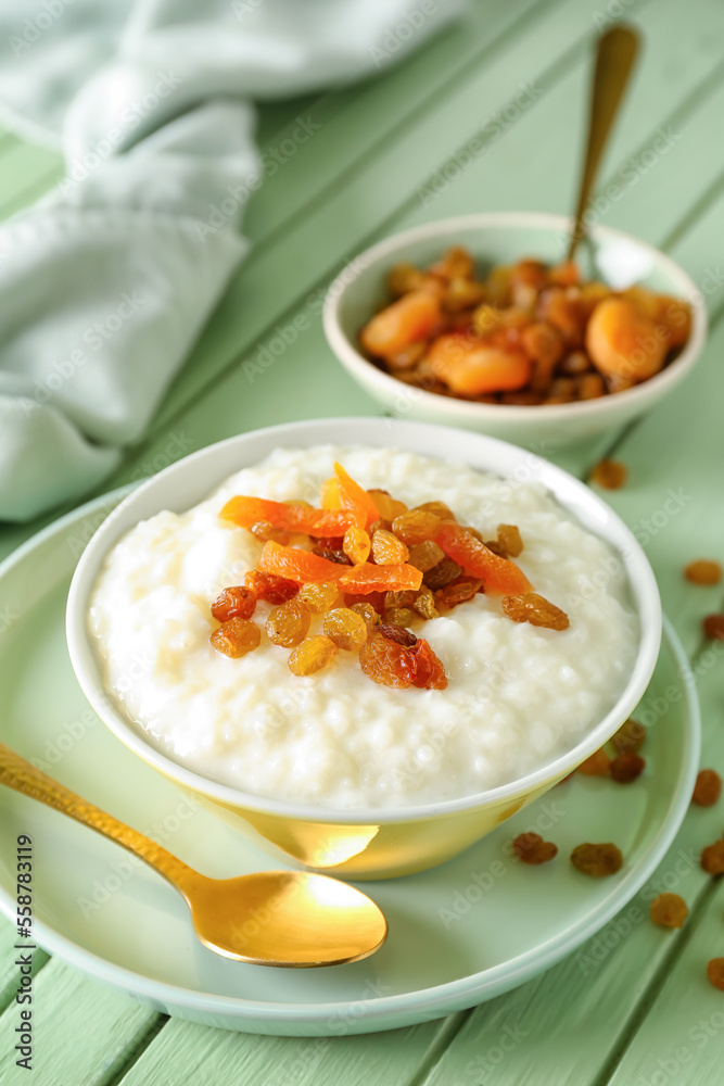 Bowl with delicious rice pudding, raisins, dried apricot and spoon on green wooden table