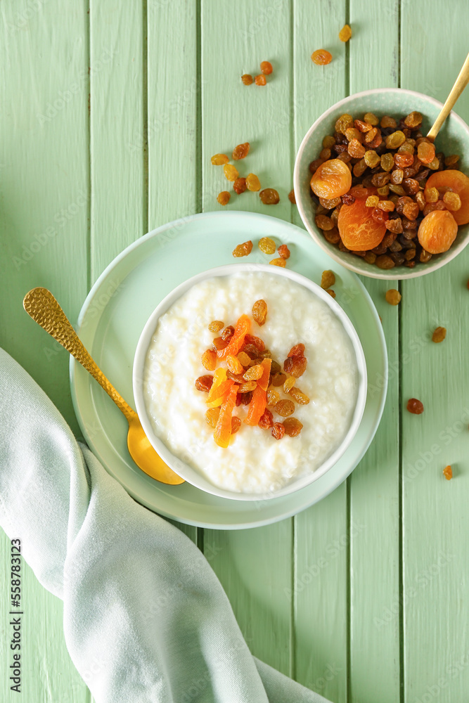 Bowl with delicious rice pudding, raisins, dried apricot and spoon on green wooden table