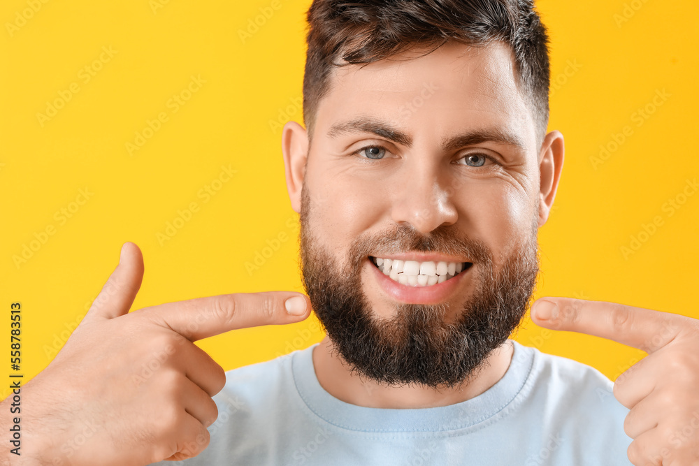 Young man pointing at his teeth on yellow background, closeup