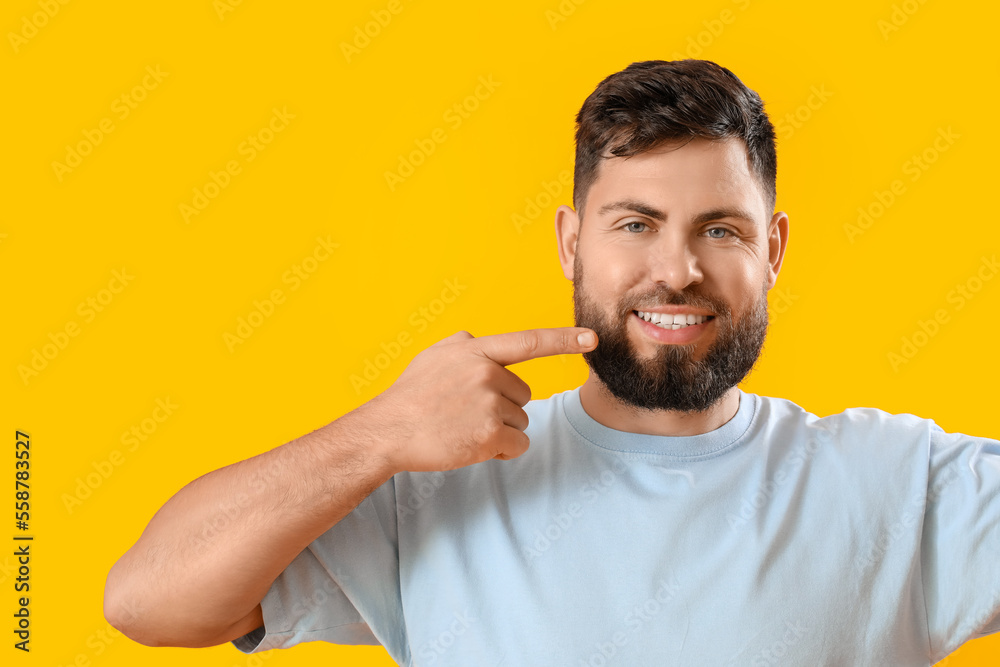 Young man pointing at his teeth on yellow background