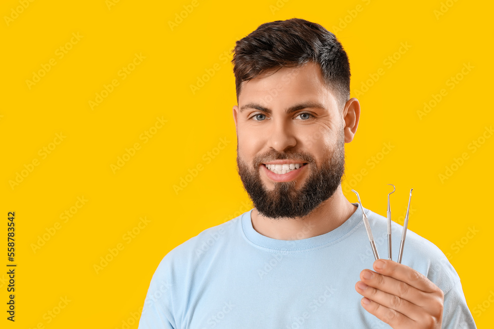 Young man with dental tools on yellow background