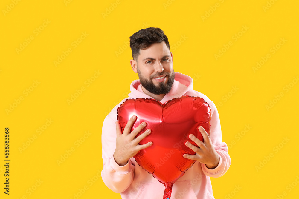 Young bearded man with balloon for Valentines Day on yellow background