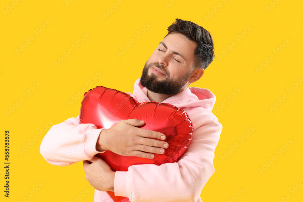 Young bearded man with balloon for Valentines Day on yellow background