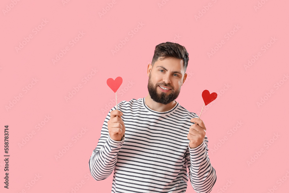 Young bearded man with paper hearts for Valentines Day on pink background